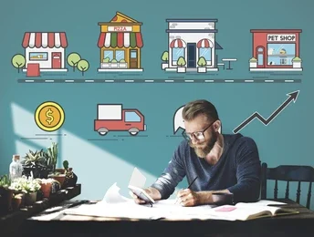A person sits at a table studying a book, with decorative icons of shops and a delivery truck on a teal wall behind them.