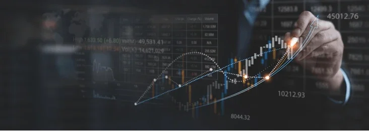 A close-up of a businessman analyzing stock market data displays a hand drawing an upward trend line on digital graphs.
